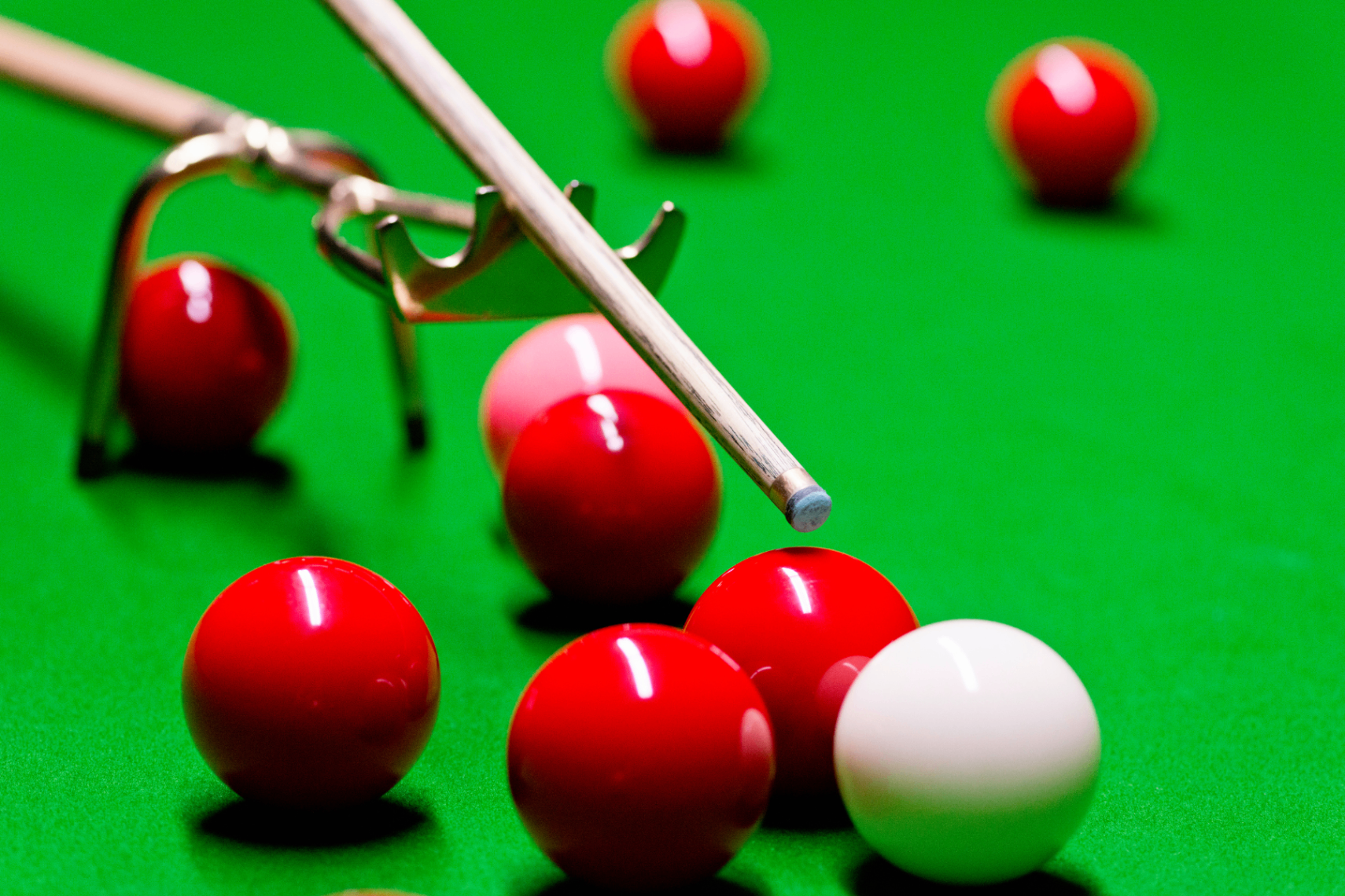 Close-up of a snooker table with red and coloured balls and a wooden cue under warm lighting